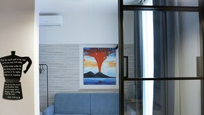 Habitació amb un sofà blau, un quadre amb un arbre i una porta corredissa de vidre.