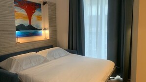 Un llit ben fet a una habitació d'hotel, amb un quadre a la paret i una finestra amb cortines.