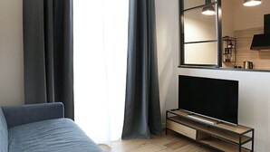 Un saló modern amb televisió de pantalla plana sobre un suport de fusta, cortines grises i un sofà gris.