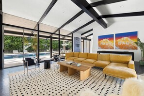 Una sala de estar moderna con un ventanal grande, una piscina y mobiliario exterior.