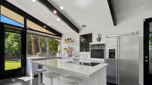 Une cuisine moderne dotée d’un grand îlot central, d’appareils électroménagers en acier inoxydable et offrant une vue sur l’extérieur.