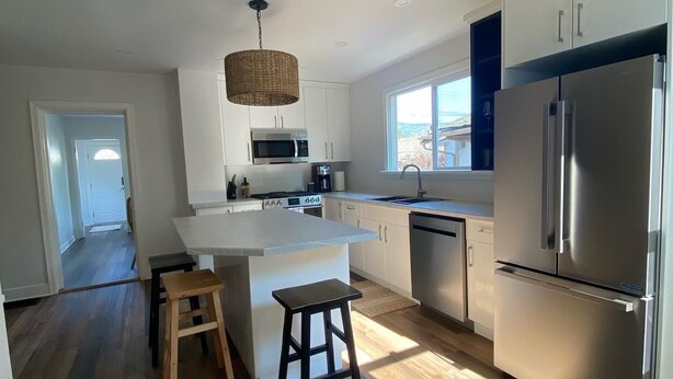 A modern kitchen with white cabinetry, a stainless steel refrigerator, a built-in oven, and a large island with stools.