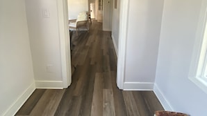 A hallway with a patterned rug, wooden flooring, and white walls.