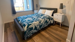 A bedroom with a bed, a nightstand, a lamp, a window with curtains, and a view of the outside.