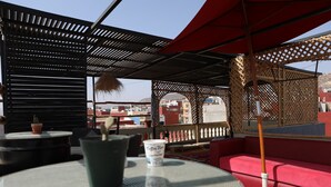 Une terrasse sur le toit avec un coin salon doté de sièges rembourrés rouges, une table ronde ornée d’un pot de fleurs et d’un gobelet jetable, et une vue sur les bâtiments en arrière-plan.