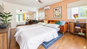 A spacious bedroom with a large bed, a desk, and a chair. There is a ceiling fan, a window with a view, and a plant.
