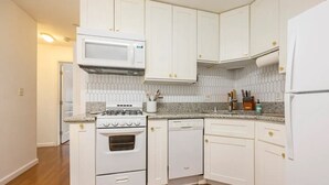 A compact kitchen with white cabinets, a microwave, a stove, and a dishwasher.