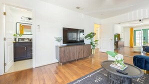 A modern living room with a flat-screen TV, dark wood flooring, and a round coffee table with a remote control.