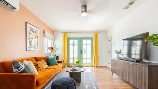 A modern living room with a sofa, a coffee table, a TV, and a large window with yellow curtains.
