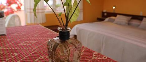 Una habitación con cama, mesita de noche y un florero con planta.