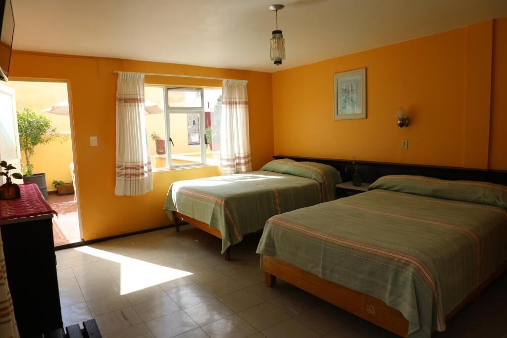 A room with two beds, a window with curtains, and a painting on the wall.