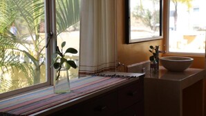 Een badkamer met een raam, een wastafel, een spiegel en een plant in een vaas.