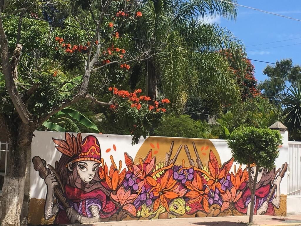 Un mural con una figura sosteniendo un báculo, rodeado de alegres diseños florales.