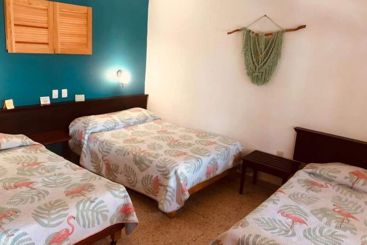 Una habitación con dos camas individuales, un cabecero de madera, una mesita pequeña y una lámpara fijada a la pared.