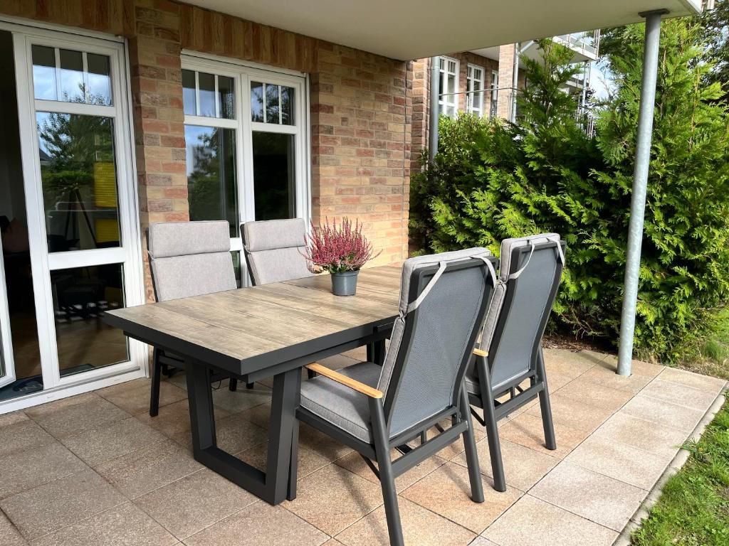 Une terrasse extérieure avec une table en bois et quatre chaises, un pot de fleurs et un mur en briques.