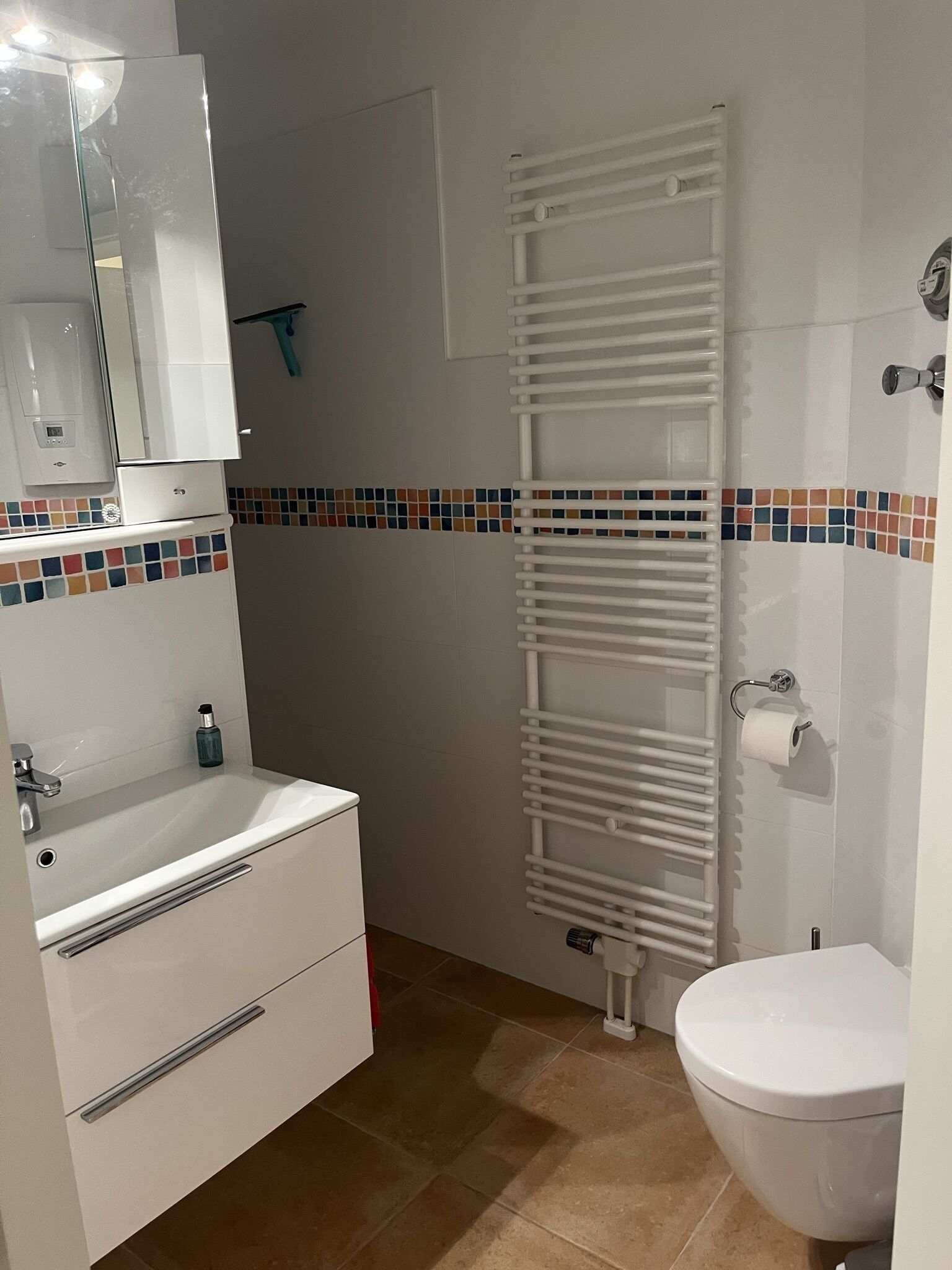 A bathroom with a white sink, mirror, and toilet. There is a towel rack and a roll of toilet paper on the wall.