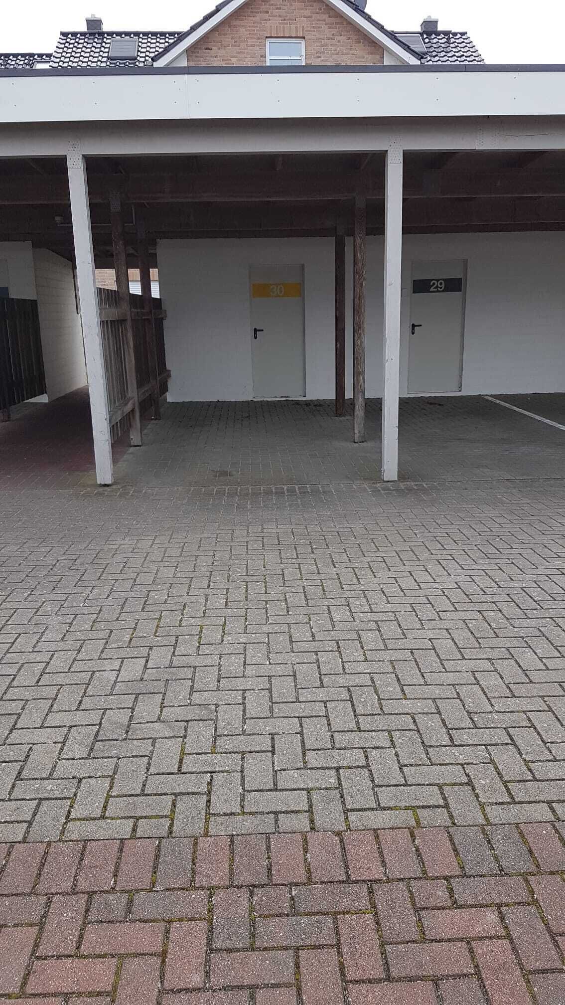 A covered parking area with a brick floor and numbered doors, likely for a hotel or similar establishment.
