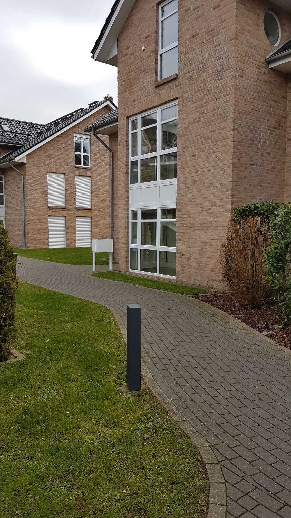 Ein modernes Gebäude mit Ziegelverkleidung, großen Fenstern und einem gepflasterten Weg.