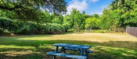 A picnic table in a grassy area with trees and a fence in the background.