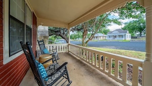 A covered porch with a white railing, two rocking chairs, and a wooden barrel.