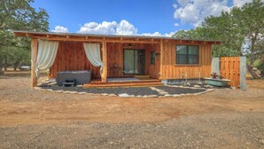 A wooden cabin with a covered porch, a hot tub, and a small outdoor seating area. - Saw Mill Cabin (Fredericksburg)