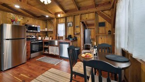 A wooden cabin interior with a kitchen, dining area, and a ceiling fan. - Saw Mill Cabin (Fredericksburg)