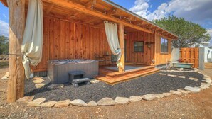 A wooden cabin with a covered porch, a hot tub, and a stone pathway. - Saw Mill Cabin (Fredericksburg)
