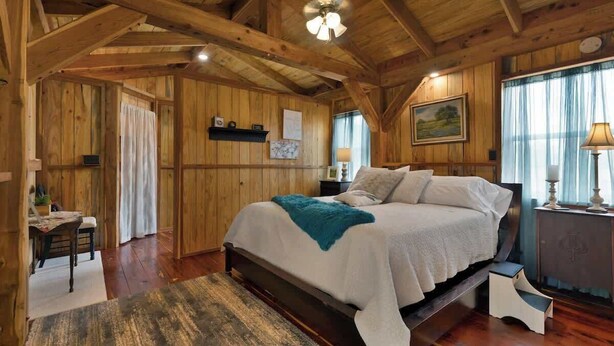A wooden cabin bedroom with a large bed, a desk, and a chair. - Saw Mill Cabin (Fredericksburg)