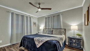 Ein Schlafzimmer mit einem Bett, zwei Nachttischen, einem Deckenventilator und einem Beistelltisch mit Lampe.
