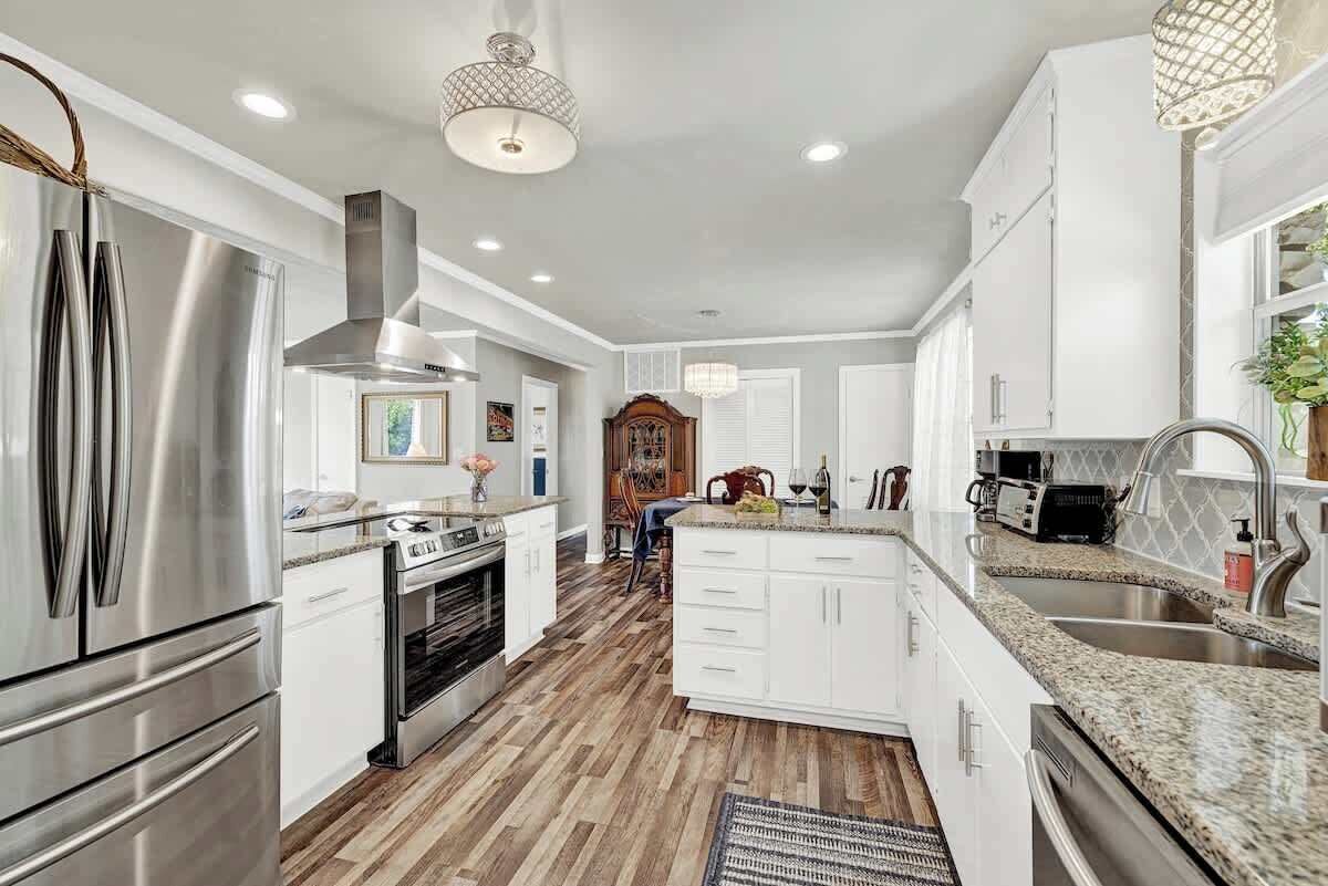 A modern kitchen with stainless steel appliances, white cabinetry, and a wooden floor.