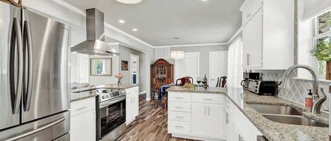 A modern kitchen with stainless steel appliances, white cabinetry, and a wooden floor.