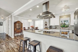 A spacious kitchen with a large island, wooden bar stools, a classic grandfather clock, and modern appliances.