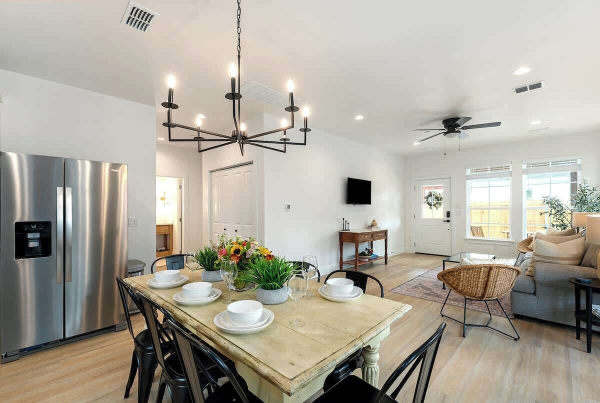 A modern kitchen with a stainless steel refrigerator, a wooden dining table set with plates and glasses, and a chandelier.