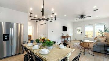 A modern kitchen with a stainless steel refrigerator, a wooden dining table set with plates and glasses, and a chandelier.