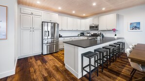 Una cocina moderna con armarios blancos, electrodomésticos de acero inoxidable y techo de madera.