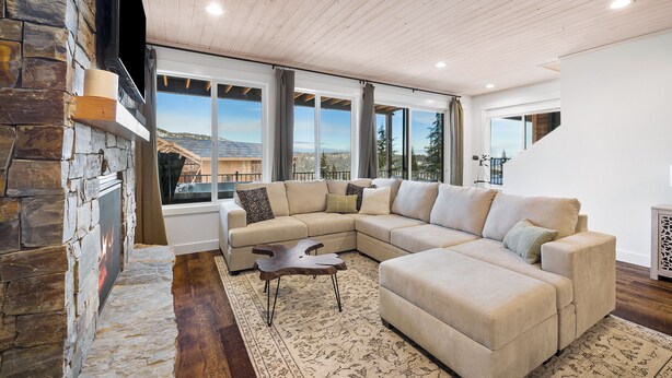 Una sala de estar moderna con chimenea de piedra, un sofá seccional beige grande y vistas al exterior.