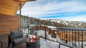 Terraza de madera con fogón y mobiliario exterior, con vistas a un paisaje nevado y edificios.