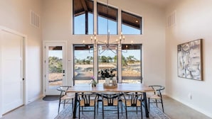 A dining area with a large table, multiple chairs, a chandelier, and large windows offering a view of the outdoors. - Johnson City Limits Home (Johnson City)