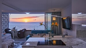 Un soggiorno moderno con un'ampia finestra vista mare, un divano, un tavolo da pranzo e un televisore montato a parete.