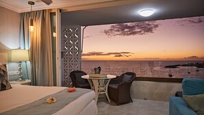 Una camera d'albergo con un letto, un tavolino con sedie, vista mare e un balcone con ringhiera.