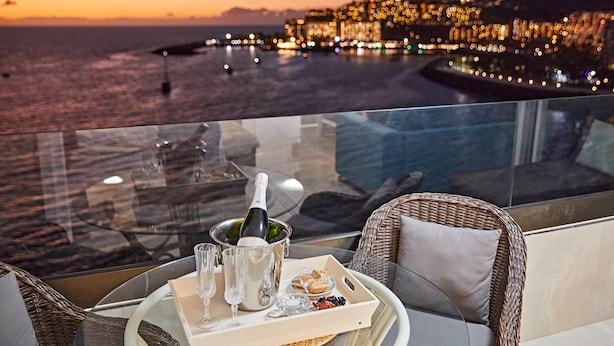 Un balcone con un tavolo apparecchiato per un pasto, con vista su una città costiera al tramonto.