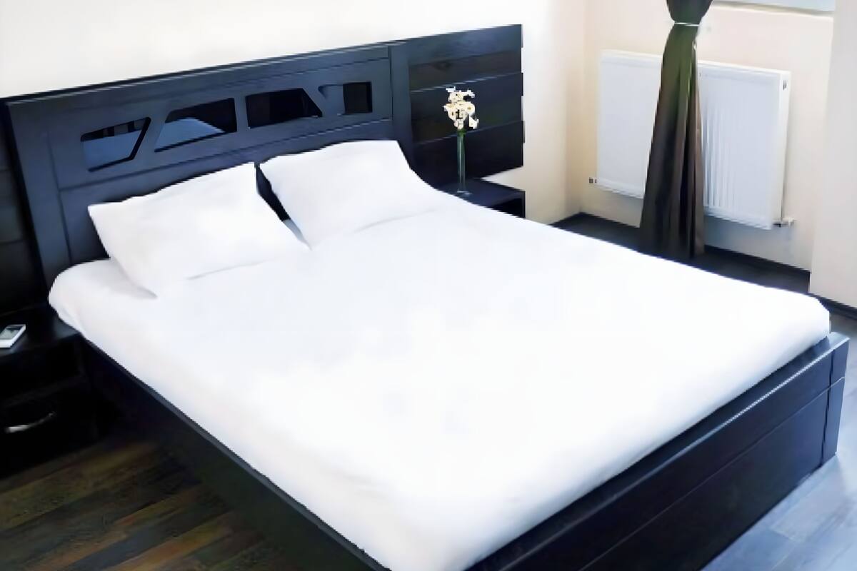 A modern bedroom with a black bed frame, white bedding, a nightstand, and a window with curtains.