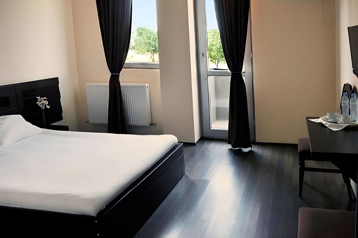 A hotel room with a bed, a desk with a chair, a radiator, and an air conditioning unit.