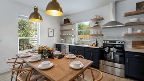 A modern kitchen with dark cabinets, a wooden dining table, and pendant lights.