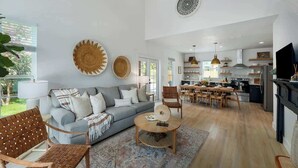 A spacious living area with a grey sofa, wooden coffee table, and a dining area with a wooden table and chairs.