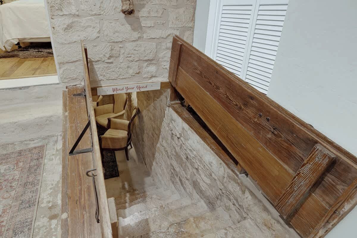 Un escalier étroit et rustique, avec un banc en bois et une pancarte sur laquelle on peut lire : « Attention à votre tête. »