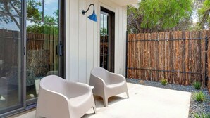 Un patio extérieur moderne avec deux chaises blanches et une lampe bleue fixée au mur.