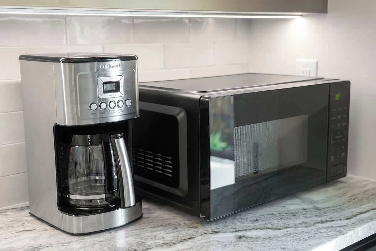 A kitchen with a coffee maker and a microwave on a marble countertop.