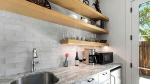 Une cuisine moderne dotée d’un plan de travail en marbre, d’un évier en acier inoxydable et d’étagères en bois au-dessus.