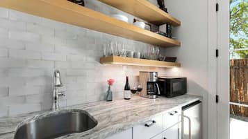 A modern kitchen with a marble countertop, stainless steel sink, and wooden shelves above.